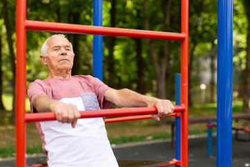 Obraz premium Elderly man doing fitness on sports ground equipment in park