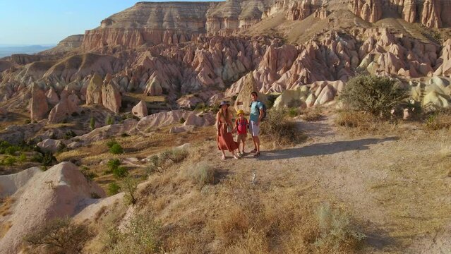 A family of tourist hike through the Red or Pink Valley near Goreme, Cappadocia. The landscape, painted in warm tones, showcases the unique geological formations and fairy chimneys that define the