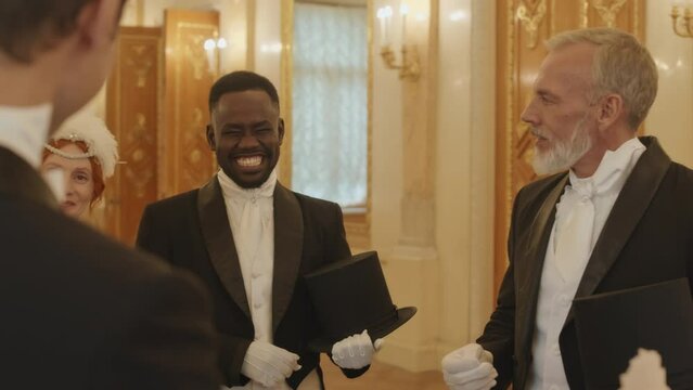 Arc shot of diverse group of aristocratic people in gala dresses and suits having small talk conversation in pompous ball hall corridor