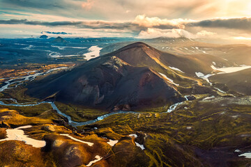 Sunset shines over volcanic mountain with river  flowing in Icelandic Highlands during summer at Iceland