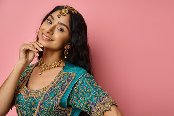 jolly indian female model with accessories in blue sari posing on pink backdrop with hand near face