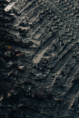 dark muddy road background with tire traces, dirty ground and autumn leaves