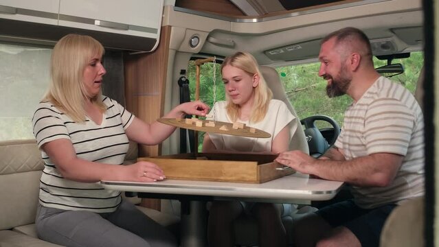 A family of three plays a board game sitting in a motorhome