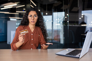 Portrait of disappointed upset woman at workplace, cheated business woman looking at camera holding bank credit debit card in hands, received rejected funds transfer, negative account balance.