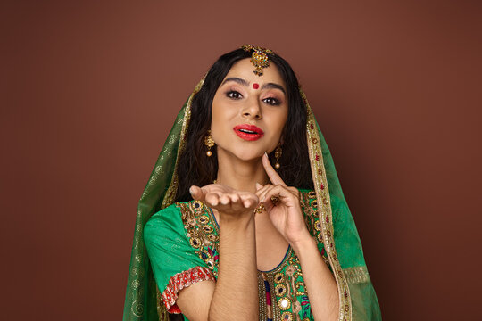 jolly indian woman in green veil with bindi dot posing with hands near face and looking at camera