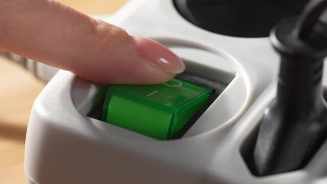 A finger presses the power switch off a surge protector. Close-up, shallow dof.