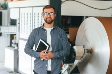 By the rounded machine for making paper. Handsome man is working at the factory of creating eco...