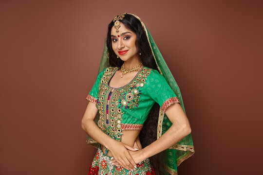 attractive cheerful indian woman with green veil and bindi dot smiling at camera on brown backdrop