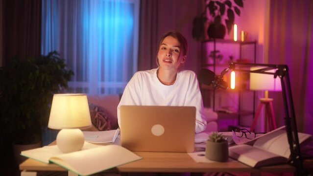 Smiling young woman influencer looking at the camera while recording video blog mobile vlog podcast live stream share experience with audience using microphone sitting at desk at home indoors