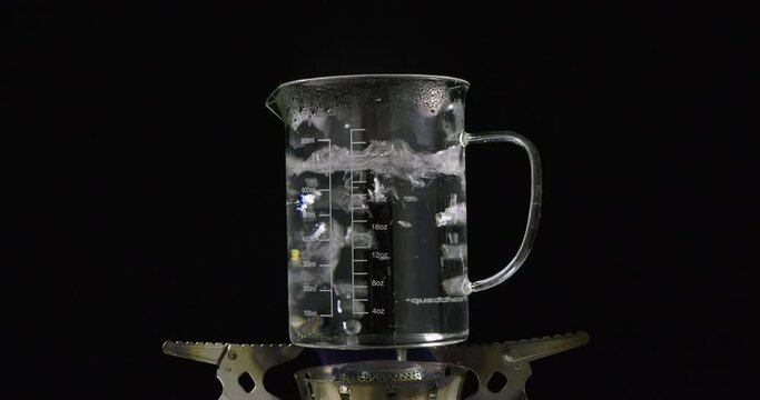 Beaker with boiling water on gas burner with black background
