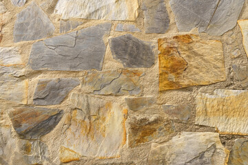 Old rough stone wall made of various square natural stones in beige, gray and brown colors.