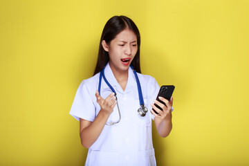 Portrait of a beautiful young woman in a yellow background, Asian woman poses with a cell phone while wearing a doctor's uniform and a stethoscope.