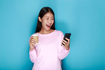 Naklejka premium Beautiful young woman in a light blue background, happy and smile, posting in stand position, A beautiful woman poses very cheerfully and happily while holding a cell phone in her other hand.