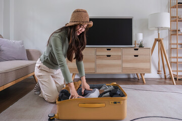 Beautiful Asian woman try to pack clothes into a yellow suitcase to prepare for a weekend getaway.
