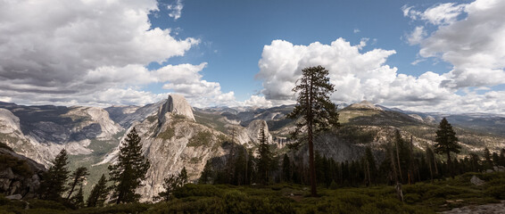 Sentinel and Half of Dome in panorama landscape of rock hills with trees and blue sky with clouds...