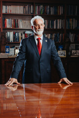 Experienced university rector in his 60s poses confidently in a library filled with books,...