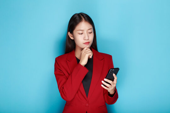 Pretty girl makes a thoughtful expression while holding a cell phone in the other hand, A woman has a pink background as a backdrop for a solo portrait.