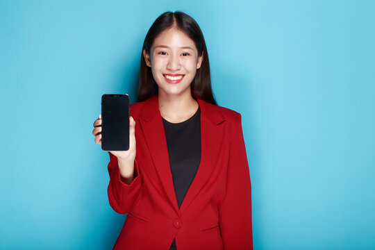 A woman has a blue background as a backdrop for a single portrait, smiling and holding a cell phone in her hand.