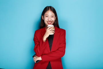 A woman has a blue background as a backdrop for a single portrait, smiling and holding a cell phone...
