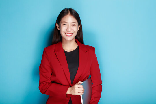 Portrait of a happy asian businesswoman working on laptop computer isolated over blue background
