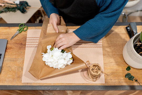 Anonymous person crafting a bouquet with white flowers and paper