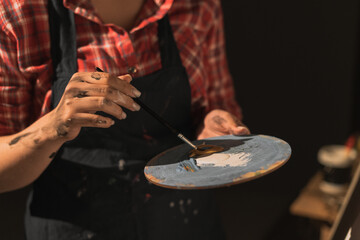 Close-up of female artist with brush mix color oil painting on palette while holding in her hands, close-up