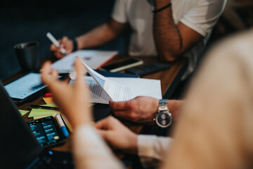 Young executives discussing project details and paperwork over coffee at a casual coffee bar. Focused on profitability and remote work opportunities in a lively indoor meeting.