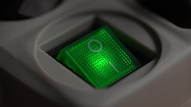 A Finger presses the Power Switch with Green Ready Light on a surge protector. Close-up, shallow dof.