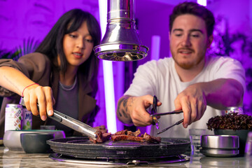 a couple in love having dinner in a Korean restaurant picking up juicy meat from the grill with...