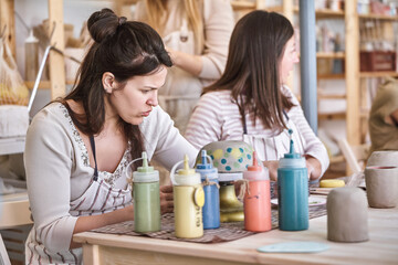 Female potter painting a handmade ceramic craft in a pottery workshop. Hobby and craft concept.