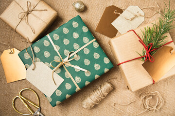 Gifts packed in Christmas beautiful paper, rope, spruce cones and scissors are on the table....