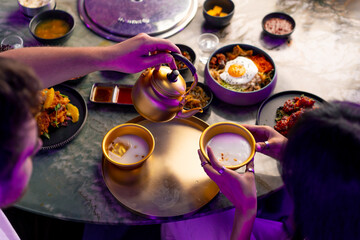 close-up of a girl pouring a traditional Korean low-alcohol drink makoli from a golden teapot into...