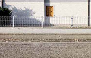 House fence made of low wall with metallic railing on top. White wall on behind, concrete sidewalk and street in front. Background for copy space