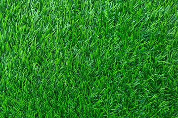 Close-up of a patch of artificial grass. The grass is green and has a smooth, plastic surface. The blades of grass are all the same length and thickness, and they are evenly spaced apart