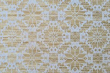 Close-up of a white fabric with a gold pattern. The fabric is smooth and silky, with a slight sheen. The gold pattern is made up of delicate swirls and flourishes
