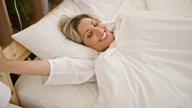 Young blonde woman waking up stretching arms at bedroom