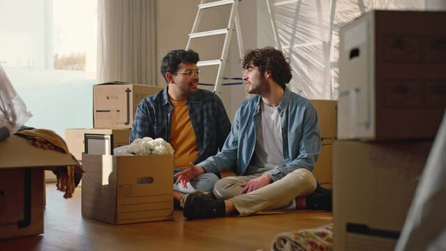Portrait of a happy multiethnic gay couple smiling looking at camera, in a new house, full of boxes.
The two boys hug each other and show the keys to the new house