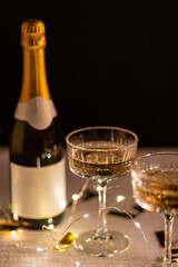 party, celebration and holidays concept - close up of champagne in glasses, electric garland lights and golden confetti on table over black background