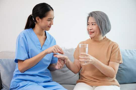 caregiver or nurse giving a pill to senior woman at home