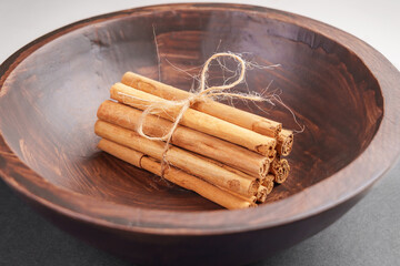 Bunch of tied cinnamon sticks with twine in wooden rustic bowl.