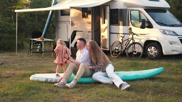 A family of three sits around a costa in the evening and cooks a meal. Evening relaxation near the motorhome
