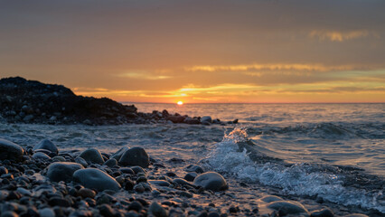 Soft sea waves washing rocky beach on sunset
