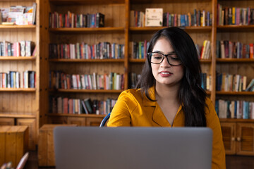 A beautiful young girl student wearing glasses or spectacles and studying in school or collage library or working in corporate office using laptop searching for information on internet or books