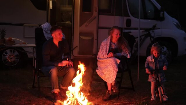 In the evening, the family sits near the campfire and warms up enjoying drinks. Evening rest near the motorhome