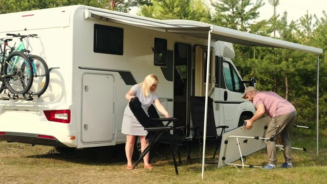 A man and a woman spread out outside a motorhome at a summer campsite