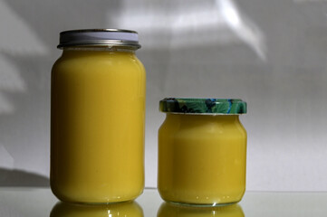 Ghee clarified butter desi in glass jar with rosemary on natural background.