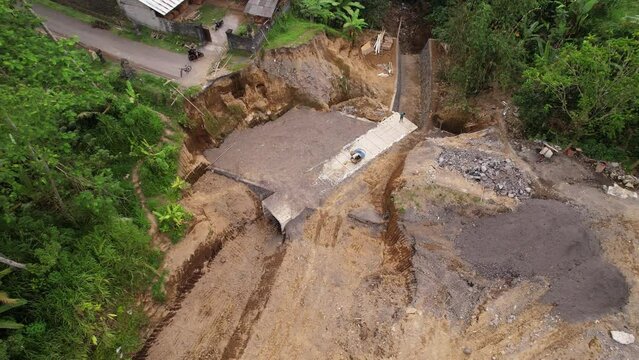 Village road restoration in rural Bali after river damage. Concrete culvert completed, slopes leveled. Aerial orbiting view of construction site with visible material heaps.