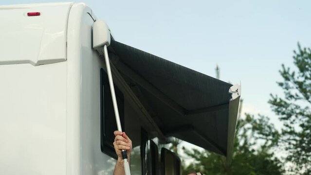A man folds the awning of a motorhome in a summer camping. Closing the awning in a mobile home
