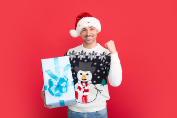 Man in Christmas sweater and Santa hat on red background. Santa with christmas gift.