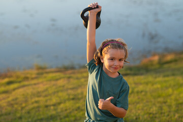 Child lifting the kettlebell in backyard outside. Kids sports exercises. Healthy kids life and sport concept. Portrait of child boy working out with dumbbells. Motivation and sport concept.